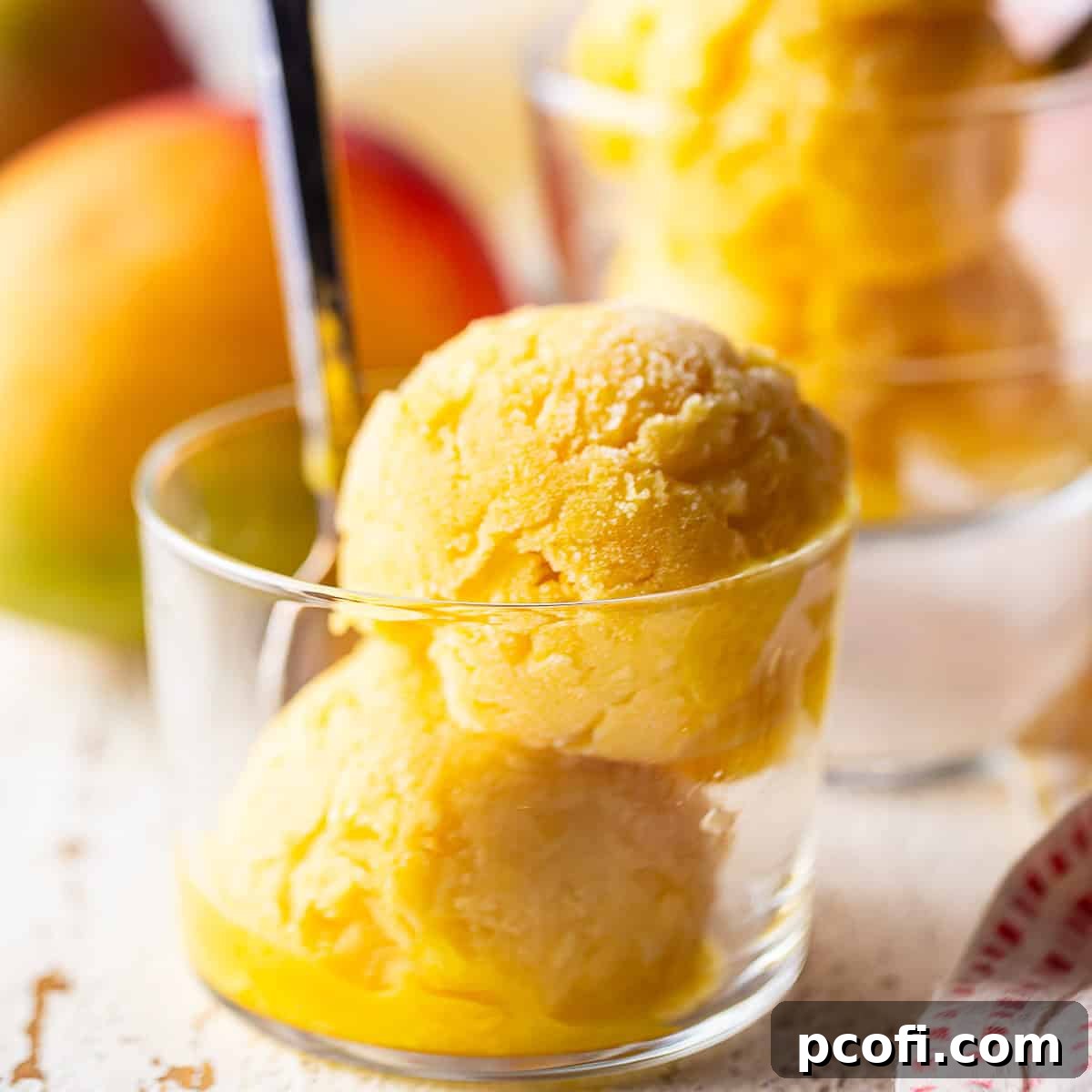 Two scoops of homemade mango sorbet in a small glass dish with a spoon, highlighting its creamy texture and vibrant color.