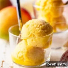 Two scoops of mango sorbet in a small glass dish with a spoon.