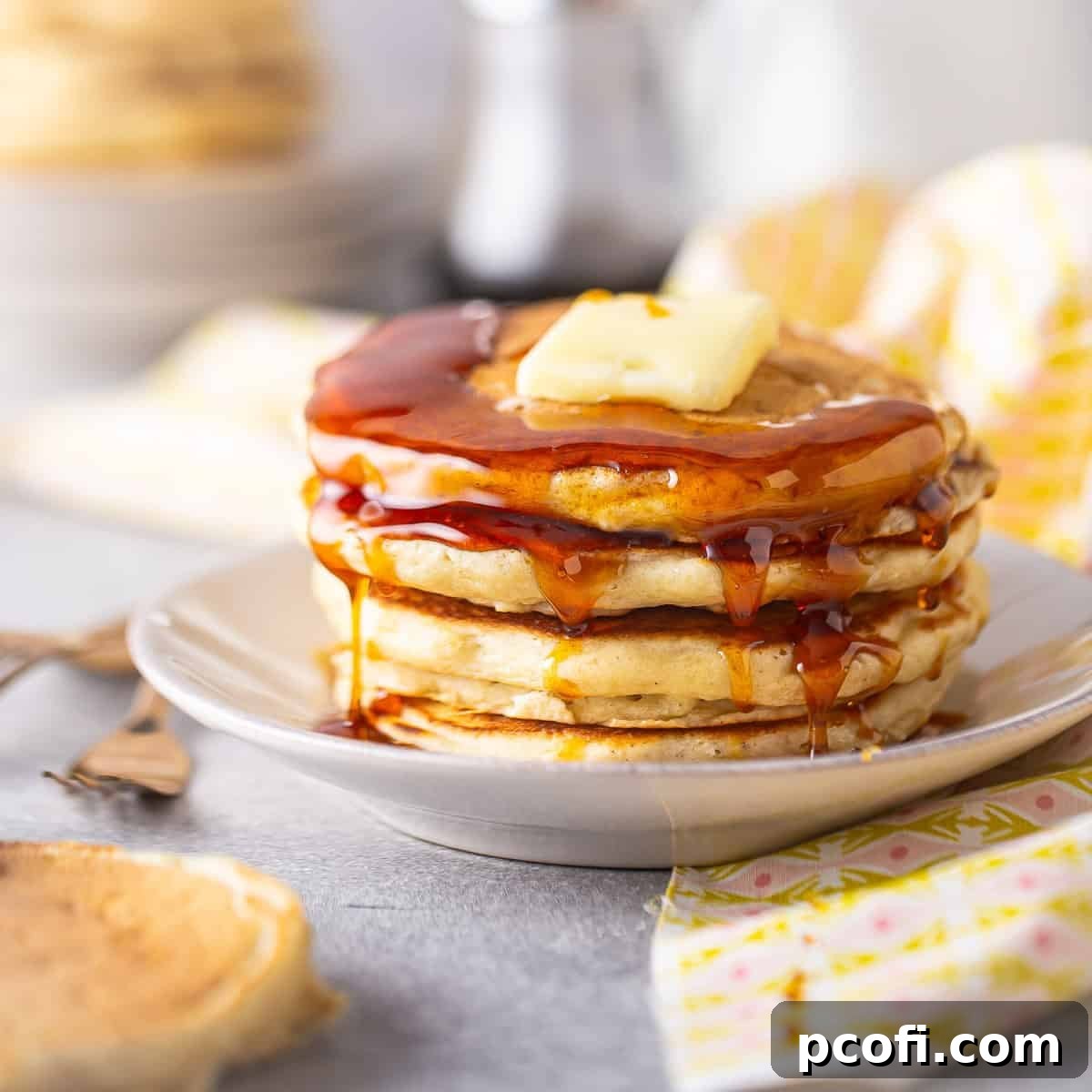 Stack of fluffy buttermilk pancakes with syrup and fruit.
