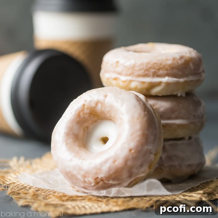 Stacks of homemade glazed sour cream donuts, with coffee cups in the background.