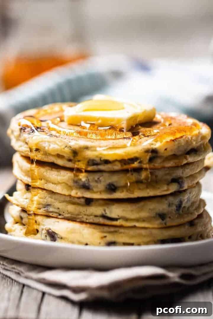 stacked chocolate chip pancakes topped with butter and syrup, ready to be eaten.