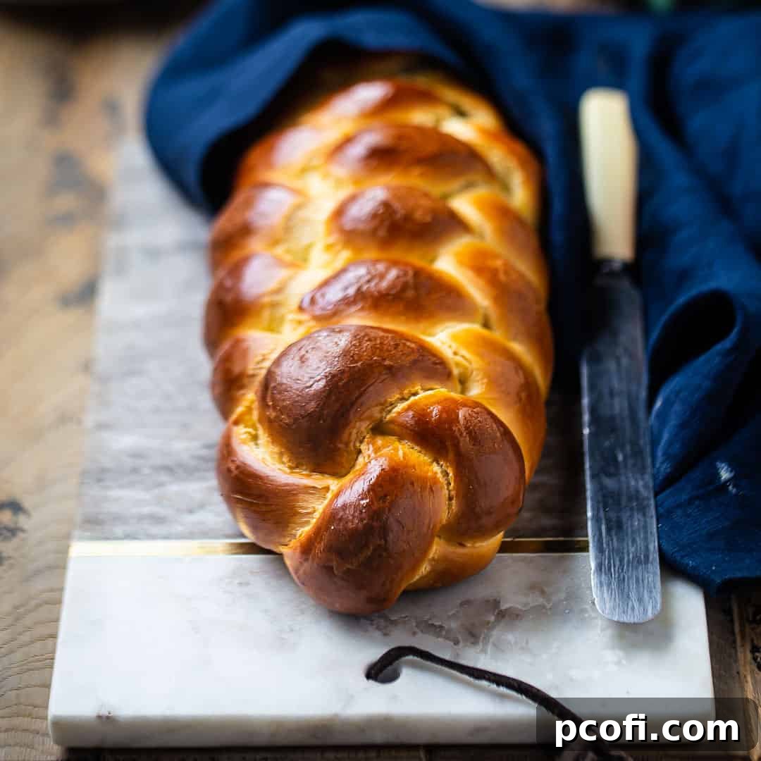 A beautifully braided challah bread rests on a marble board, accompanied by a blue cloth, ready to be served.