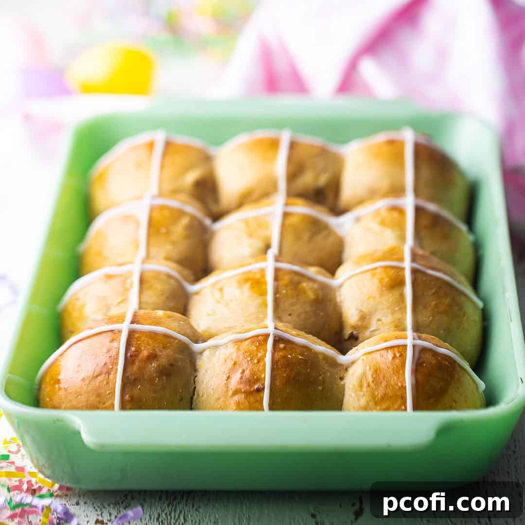 Classic hot cross buns, freshly baked in a rectangular jadeite baking dish, featuring their signature icing crosses.