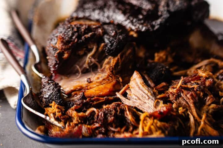 Pork roast being pulled on an enameled tray with 2 forks. 