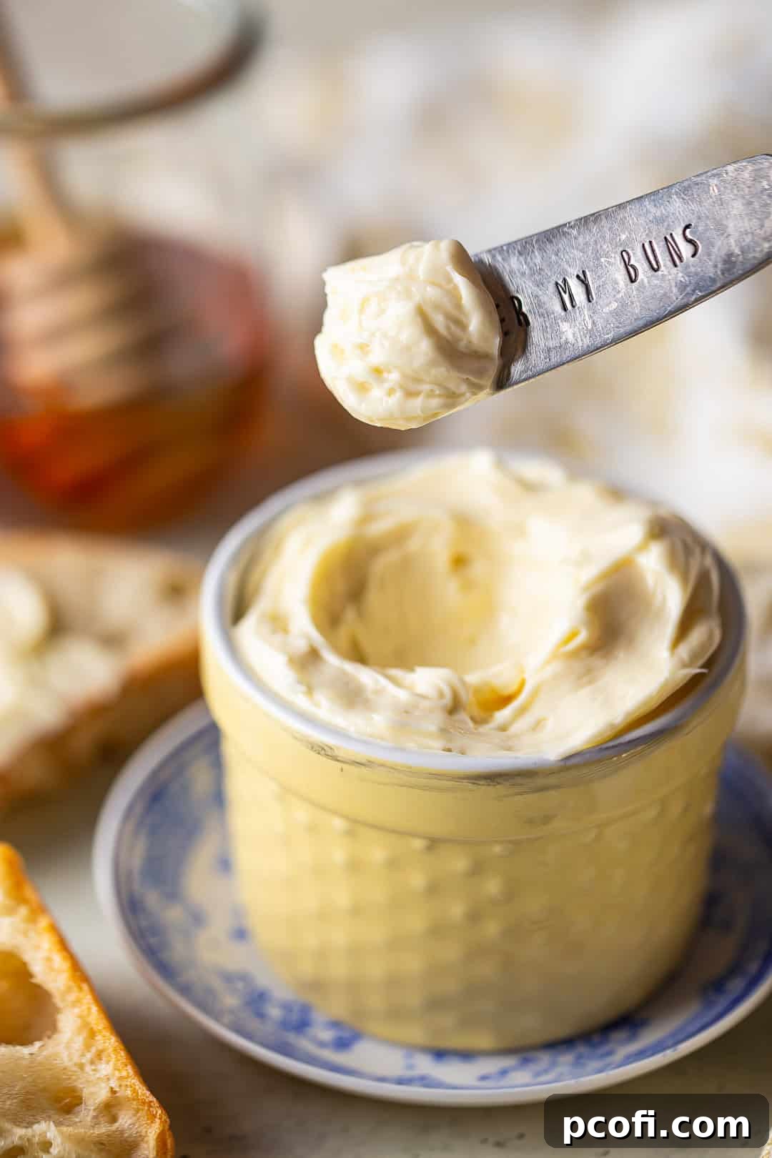 Scooping homemade honey butter from a pot with a vintage silver knife, showing its creamy texture.