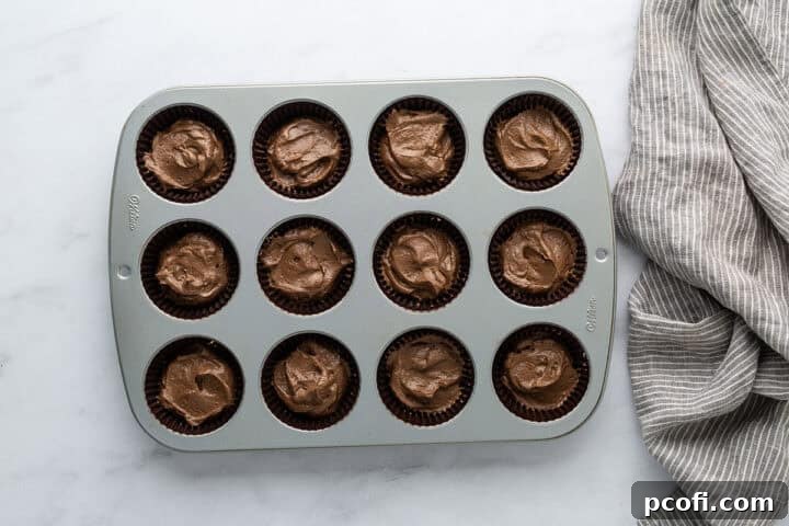 Cupcake batter neatly scooped into paper liners in a muffin pan