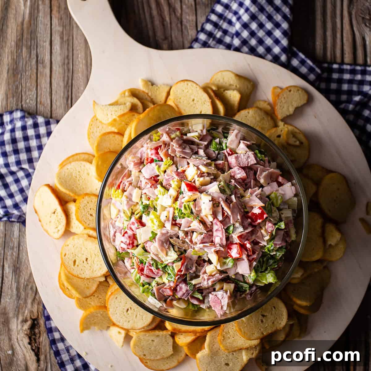A hearty bowl of hoagie dip served on a white wooden board, surrounded by crunchy bagel chips.
