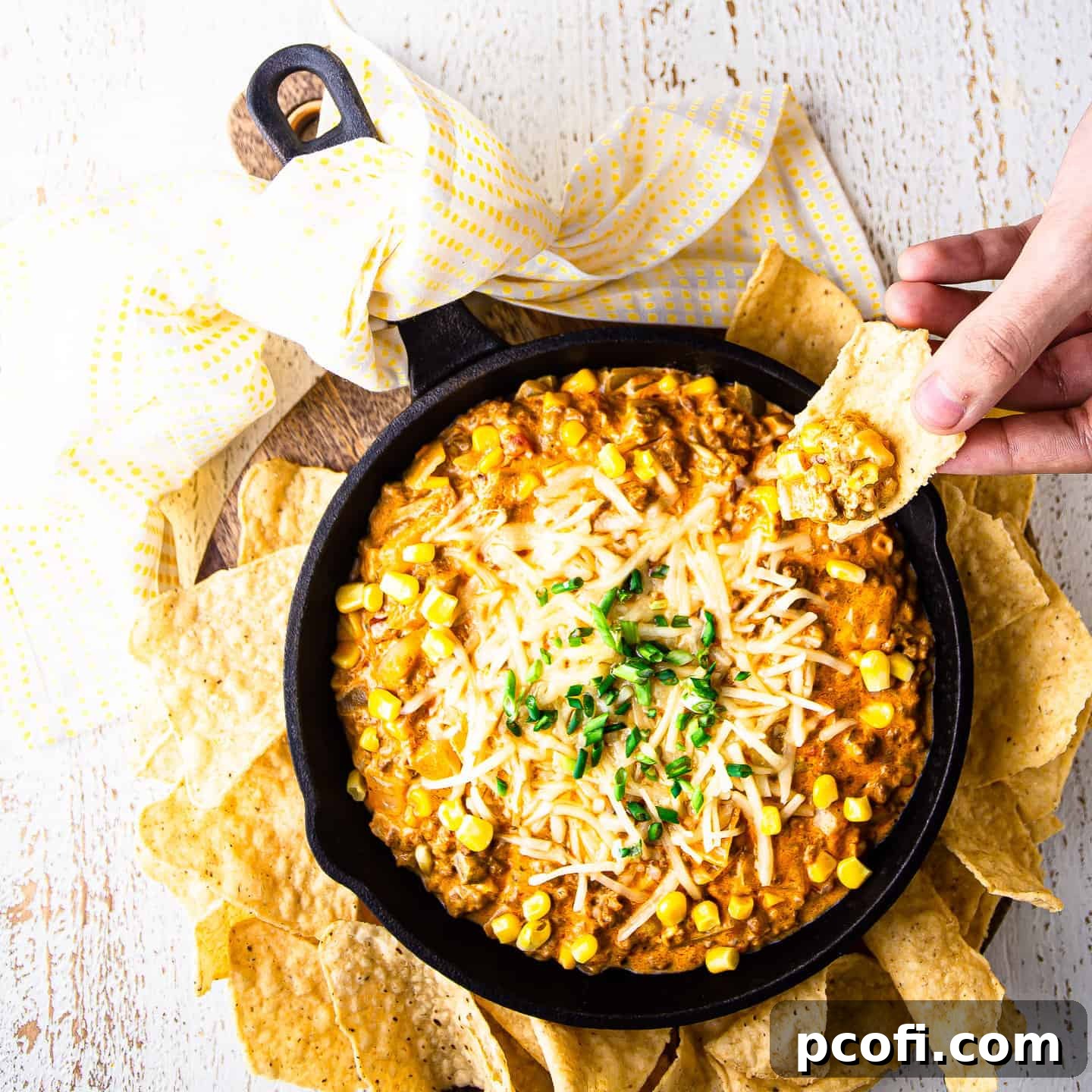 A corn chip scooping hot and cheesy corn dip from a sizzling skillet.