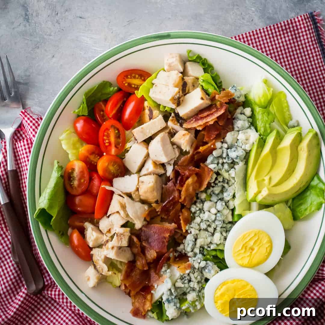 An overhead view of a colorful Cobb salad in a bowl, placed next to a red checkered napkin.