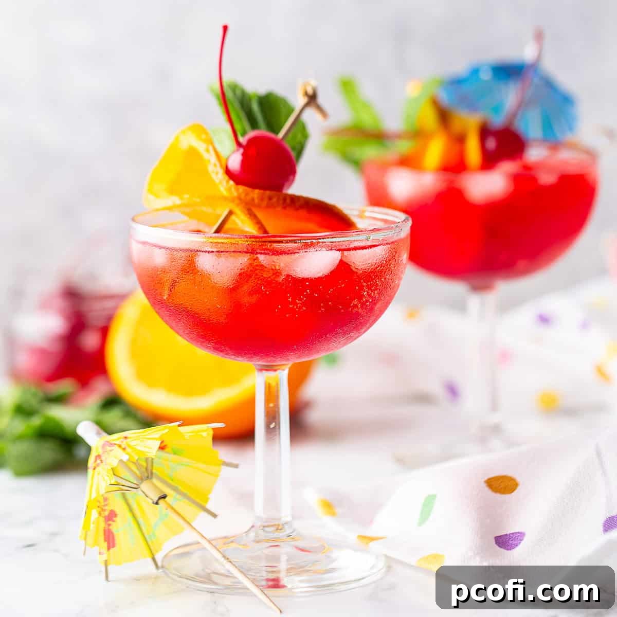 Two festive Shirley Temple drinks served in champagne coupes, garnished with orange slices, maraschino cherries, and charming paper umbrellas.