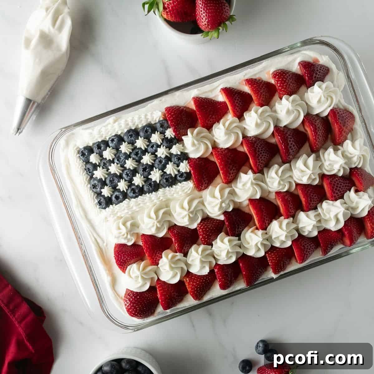 A festive American flag cake, beautifully decorated with vanilla frosting, fresh strawberries, and blueberries, presented in a baking pan.