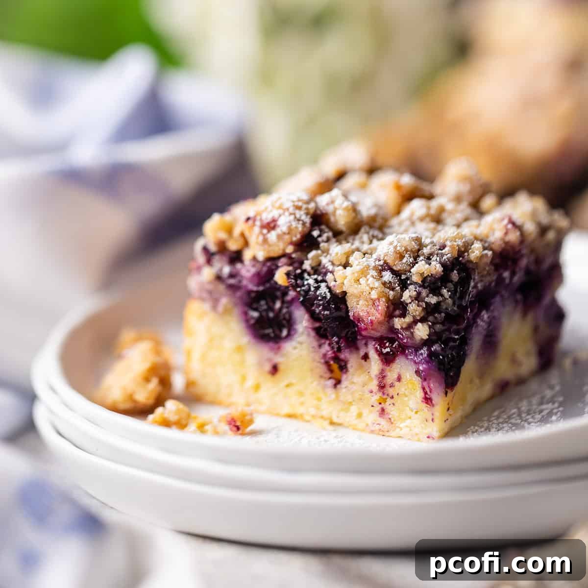 A square slice of magnificent blueberry buckle resting on a white ceramic plate.