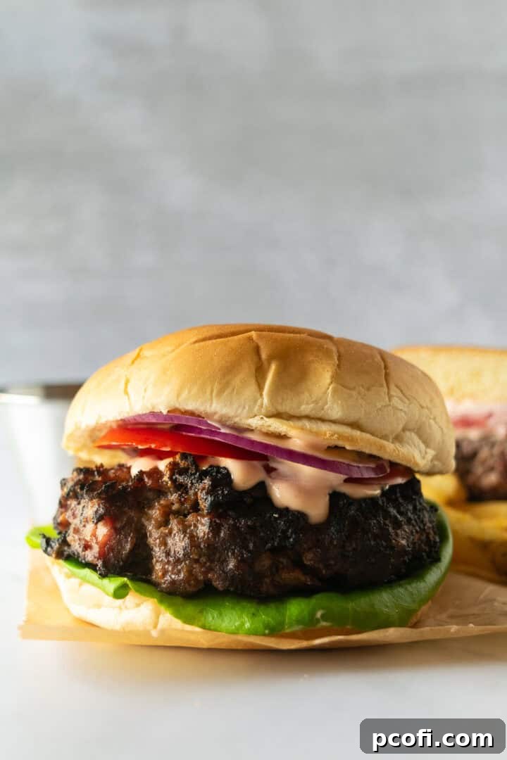 Mouth-watering bacon cheeseburgers stacked with fresh lettuce, ripe tomato slices, red onion, and a special sauce, all served on a toasted bun.