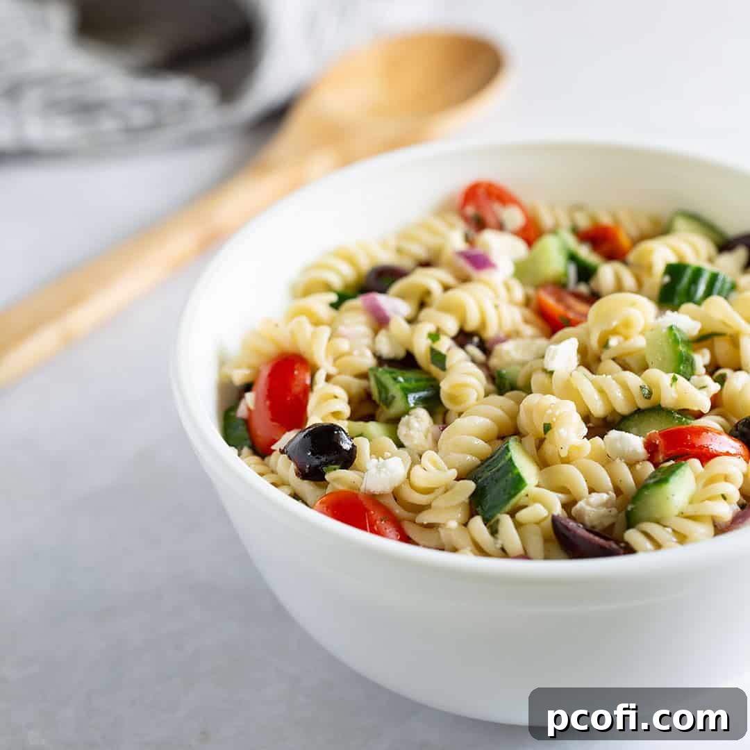A close-up view of a vibrant Greek pasta salad in a large serving bowl, featuring colorful vegetables and feta cheese.