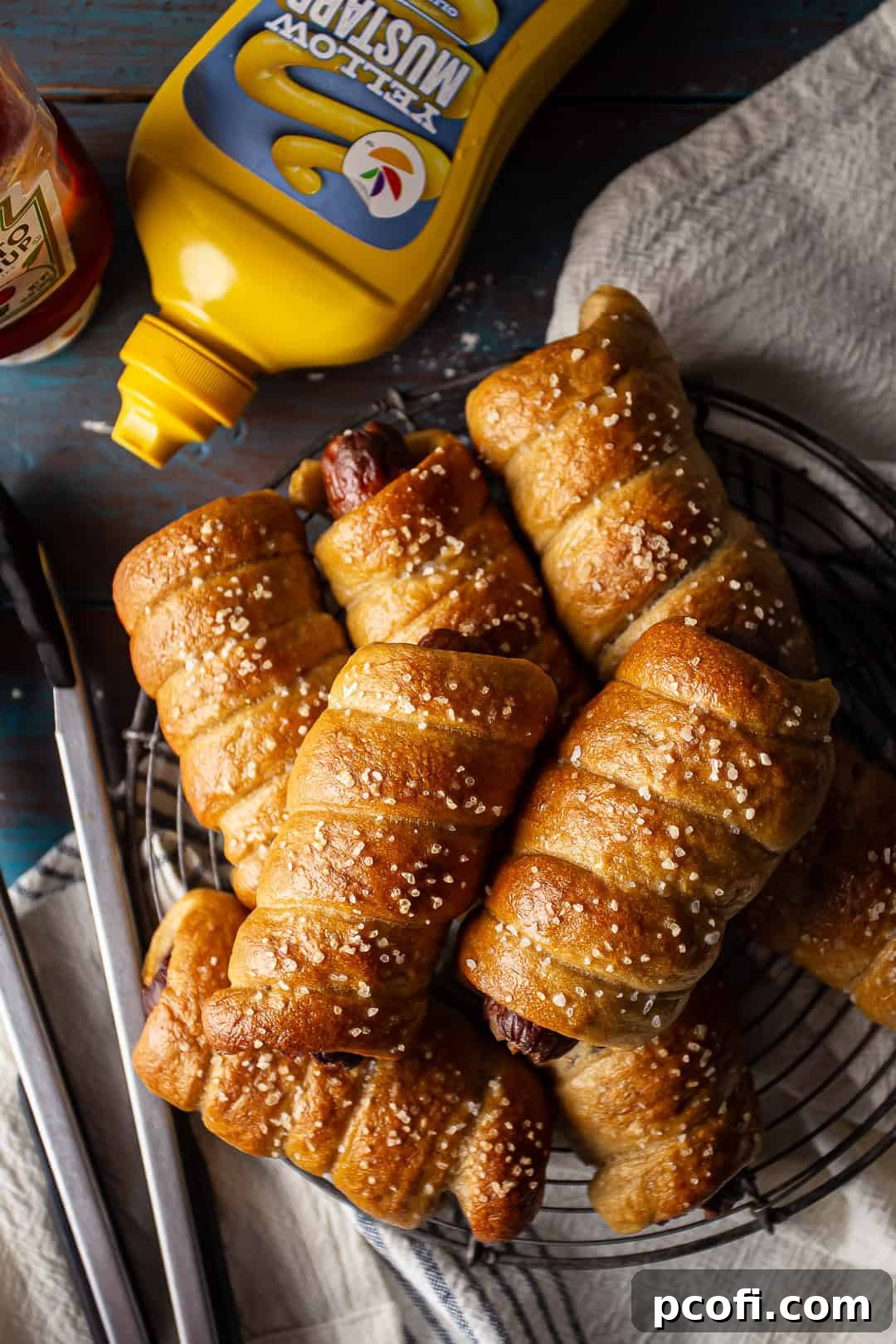 An overhead shot of a single homemade pretzel hot dog, presented with dollops of classic mustard and ketchup for dipping on a clean surface.