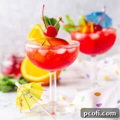 Two Shirley Temple drinks in champagne coups with orange slices, maraschino cherries, and paper umbrellas.