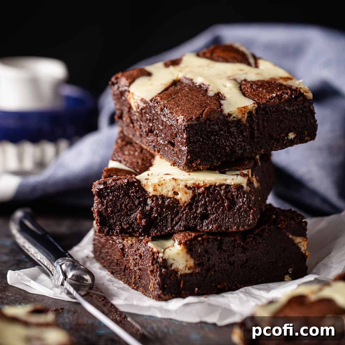 Three cheesecake brownies stacked on parchment paper, rich and marbled.