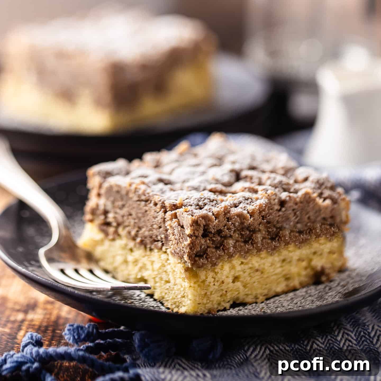 A square slice of cinnamon crumb cake on a dark plate, a classic comfort food.