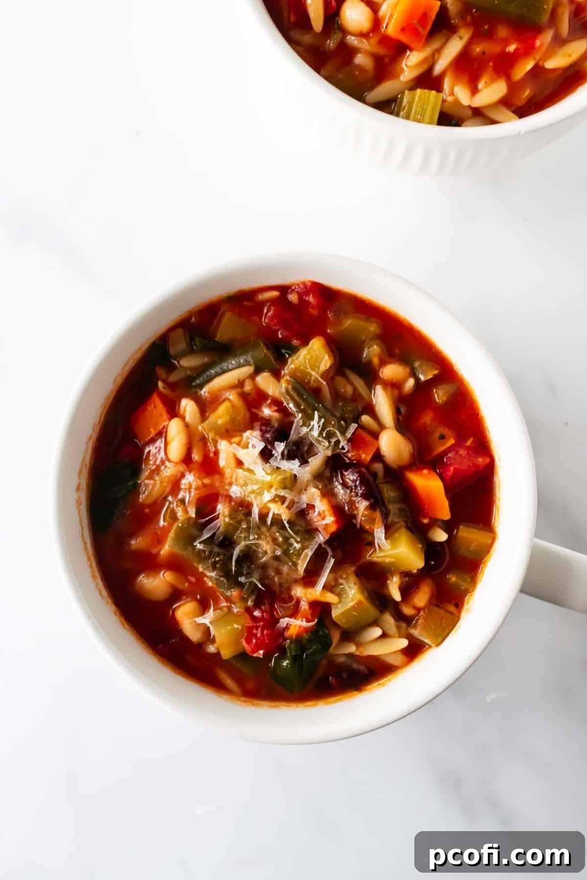 A white bowl brimming with hearty minestrone soup, generously garnished with freshly grated Parmesan cheese.