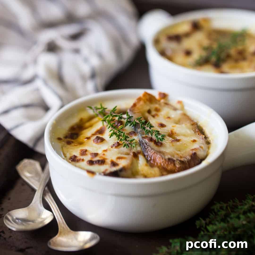 French onion soup in a white ceramic crock on a dark brown tray with vintage silver spoons.