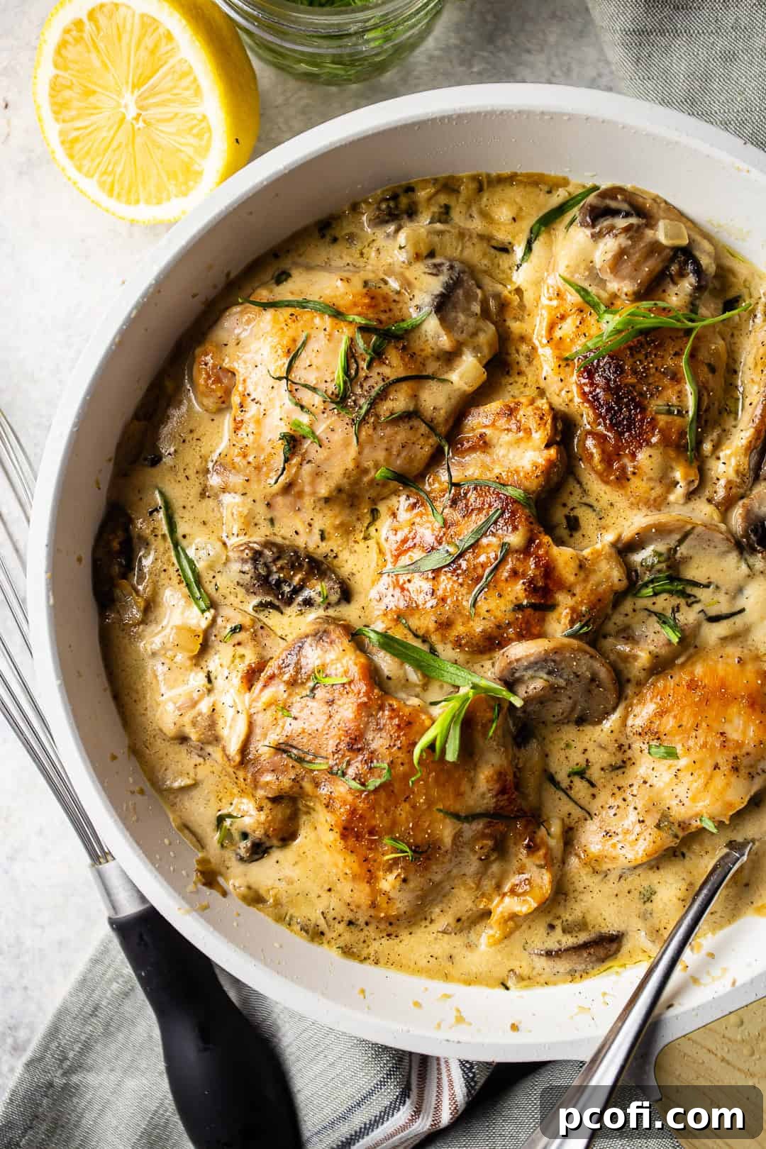 Chicken Dijon served in a pan with mushrooms, onions, herbs, and lemon wedges for garnish.