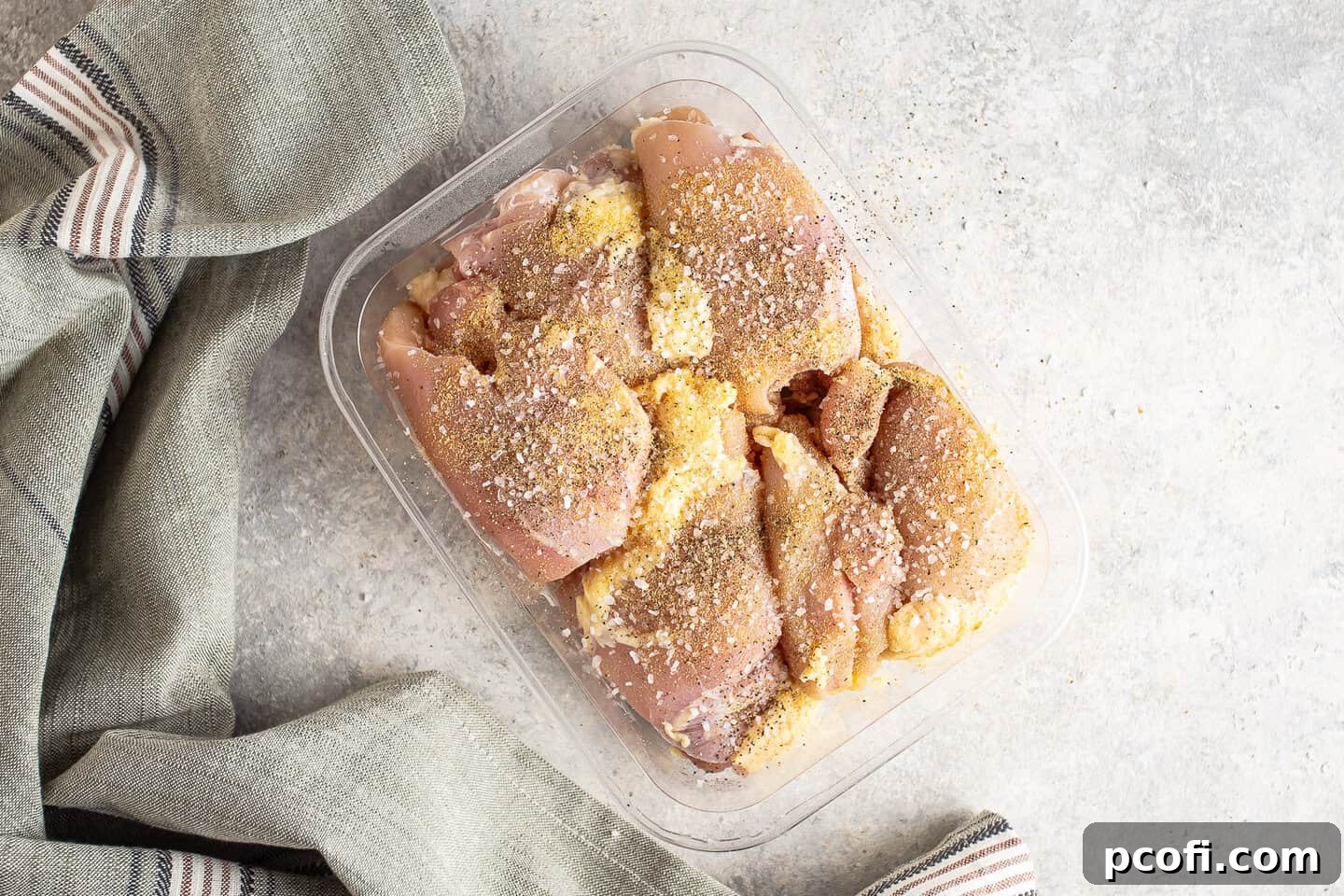 Seasoning raw chicken thighs with salt, garlic powder, and pepper.