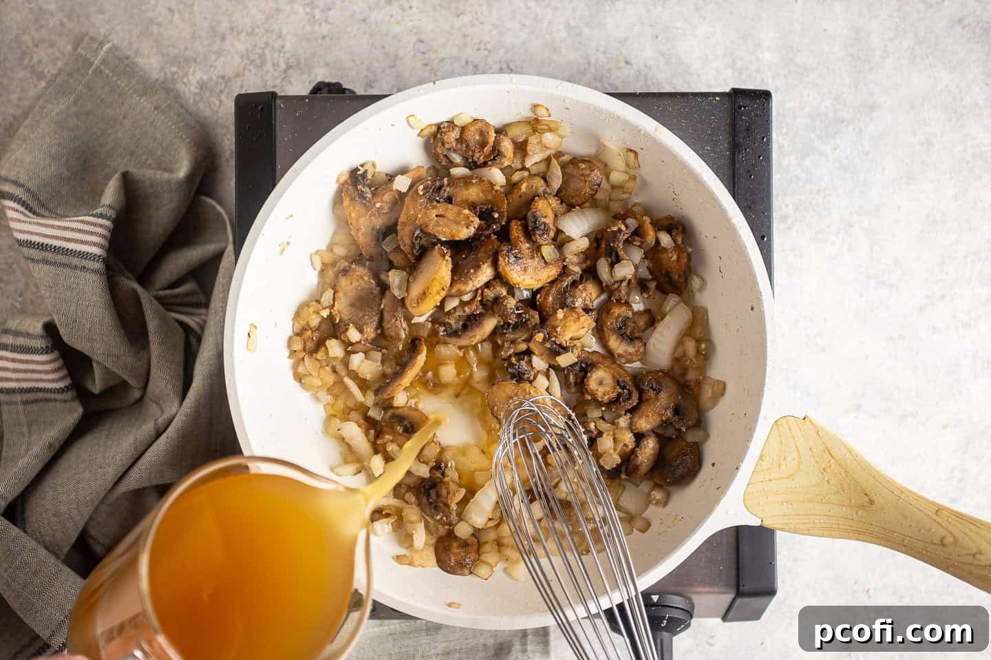 Whisking chicken stock into the flour-coated mushrooms and onions to form a sauce.