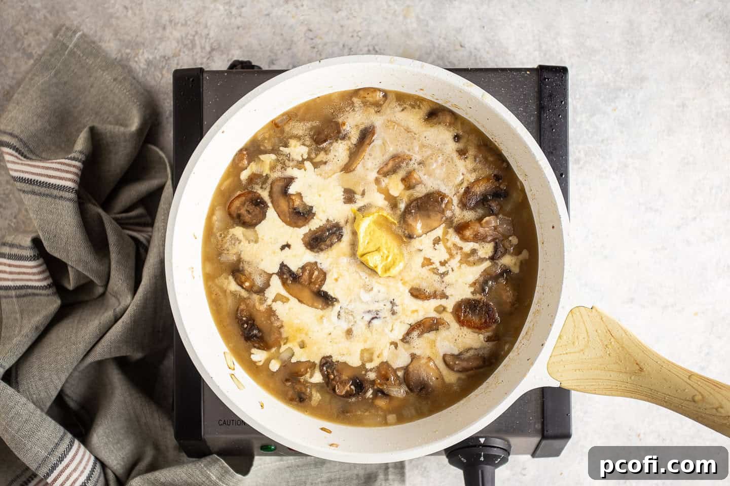 Adding heavy cream to the simmering Dijon sauce in a skillet.