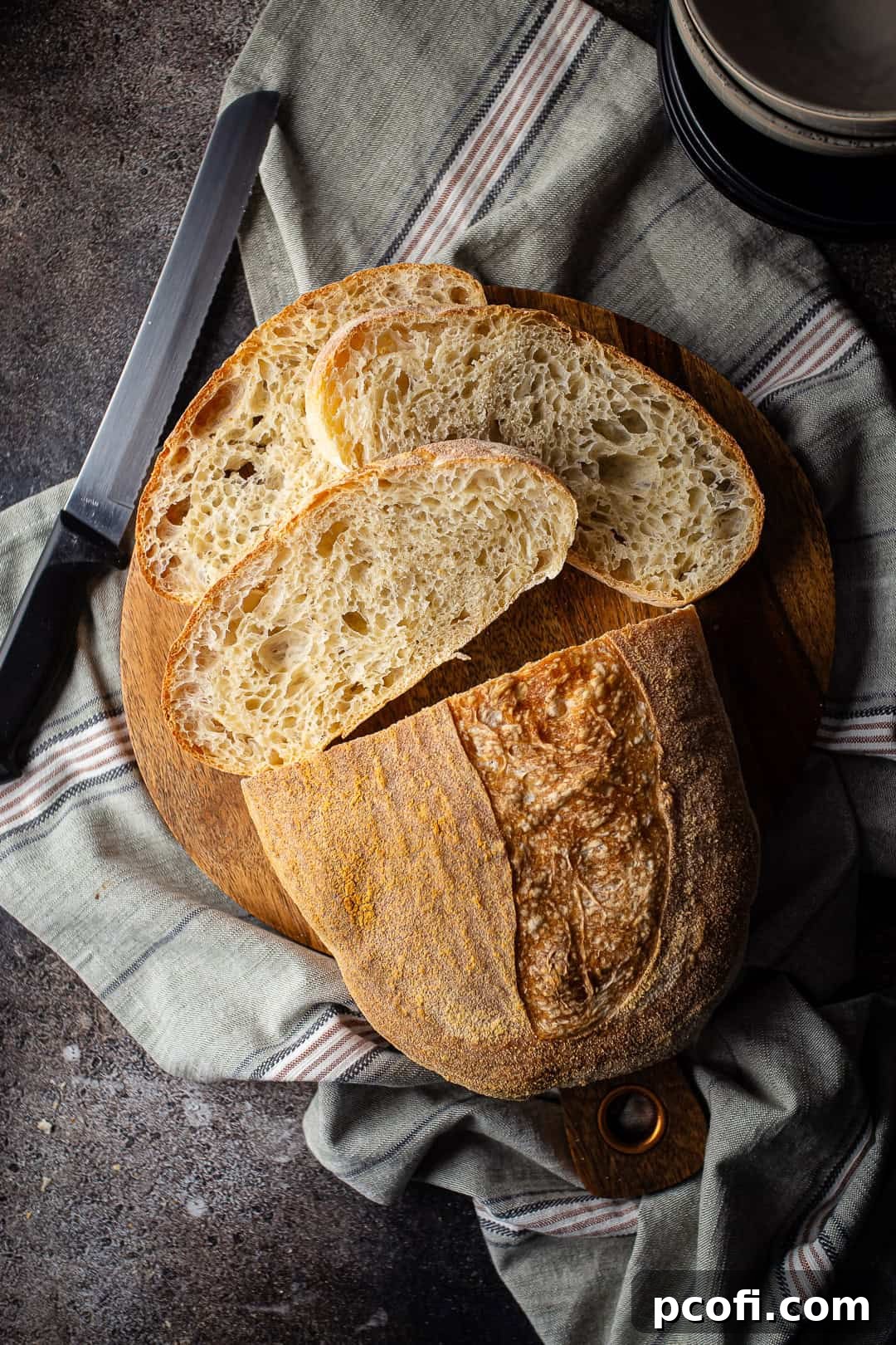 Overhead image of a beautifully crusty batard of pan de cristal bread on a wooden board.