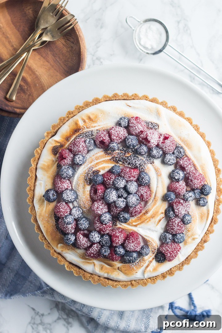 A slice of S'mores Berry Tart ready to be served, showcasing the layers of crust, chocolate cream, meringue, and fresh berries.