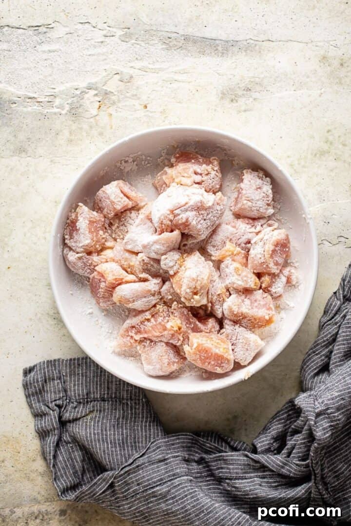 Cubed chicken seasoned with spices and generously tossed in flour, ready for cooking.