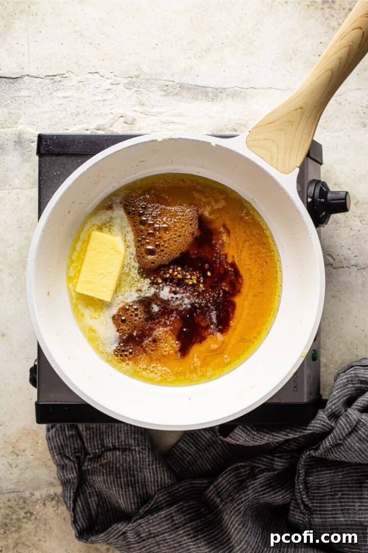 A simmering honey butter sauce with butter, honey, soy sauce, and spices in a skillet, ready for chicken.