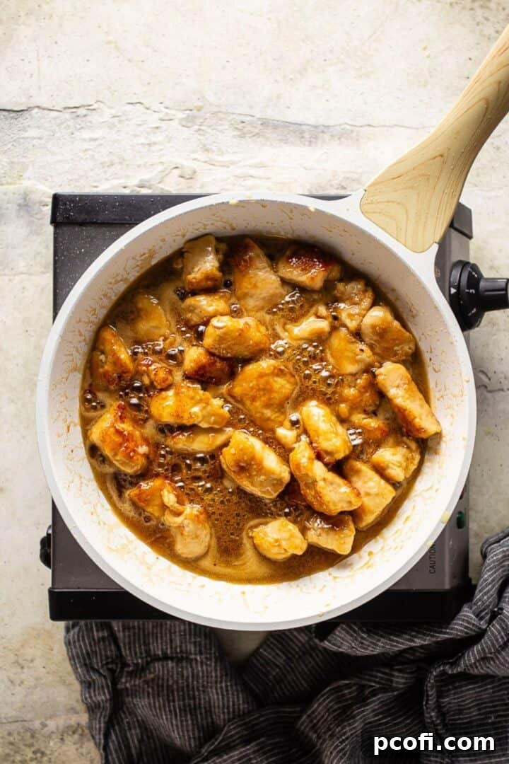 Perfectly cooked cubed chicken glistening in a rich, sticky honey butter sauce within a skillet.