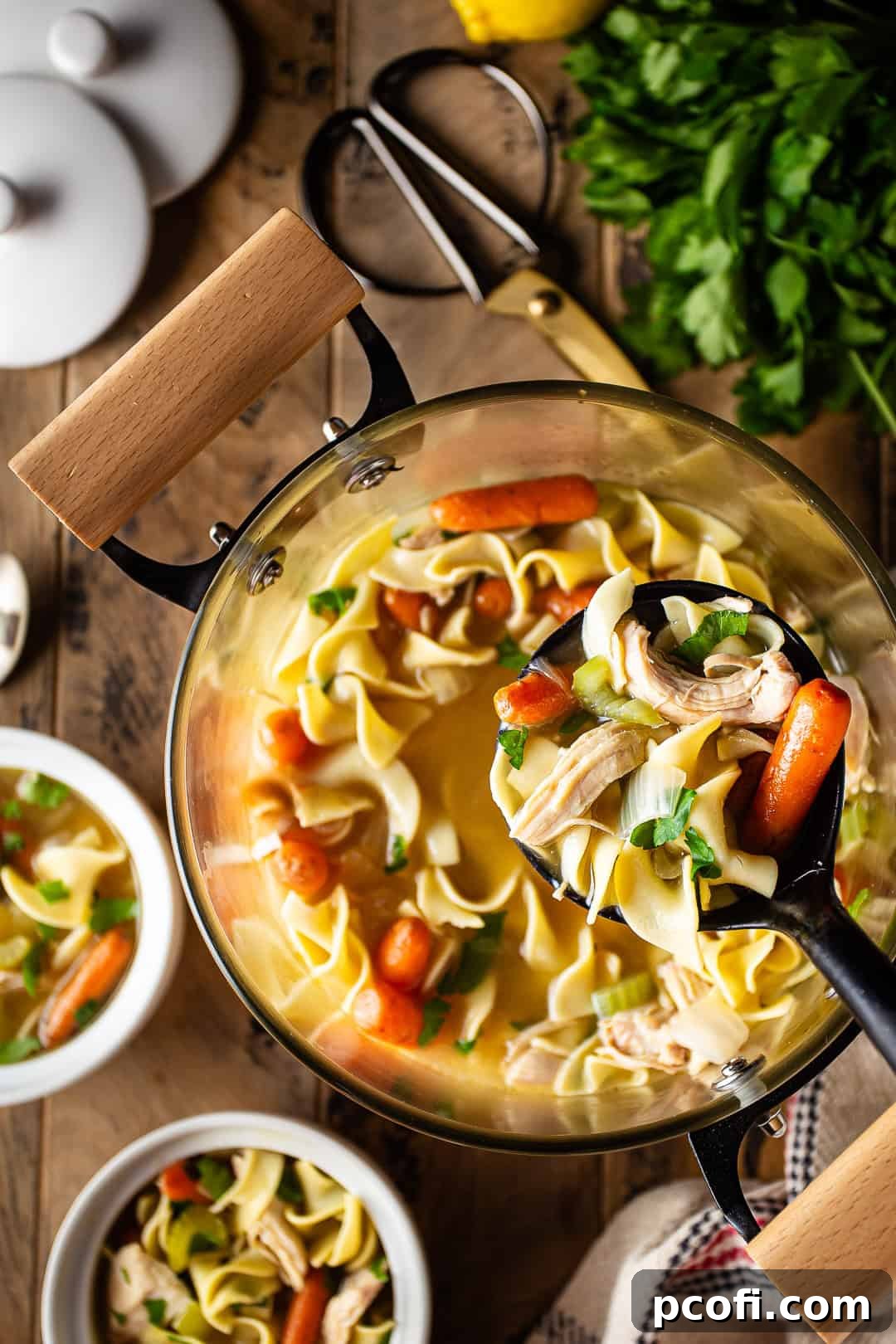 A ladle filled with homemade chicken noodle soup, showcasing tender chicken, plump noodles, and colorful vegetables.