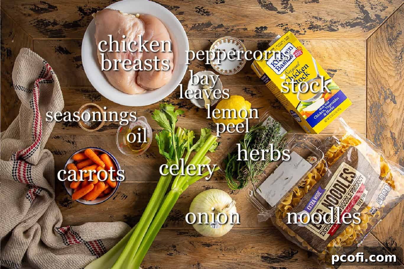 A vibrant display of fresh ingredients for chicken noodle soup, including carrots, celery, onions, chicken, and herbs.