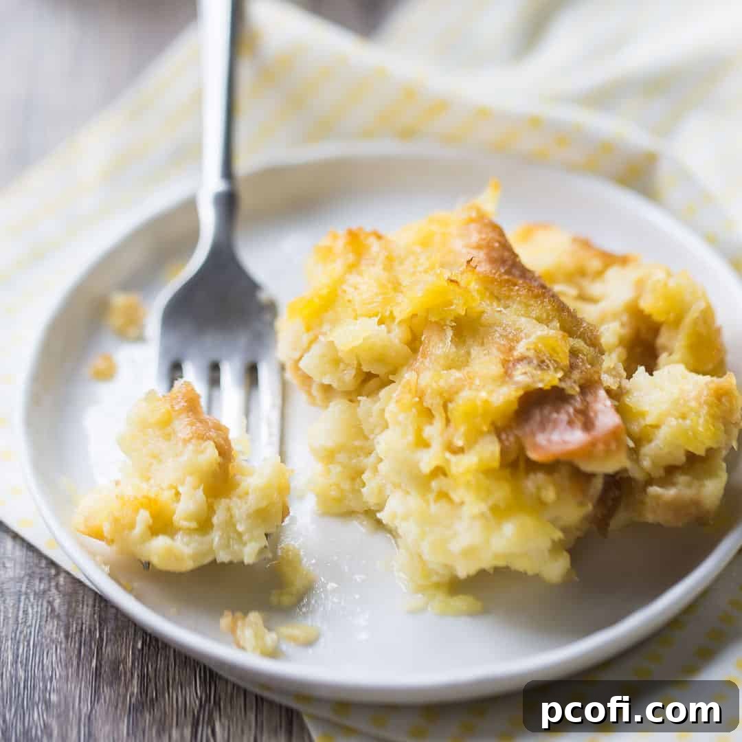A serving of baked pineapple stuffing on a small white plate, accompanied by a silver fork and a cheerful yellow printed napkin.