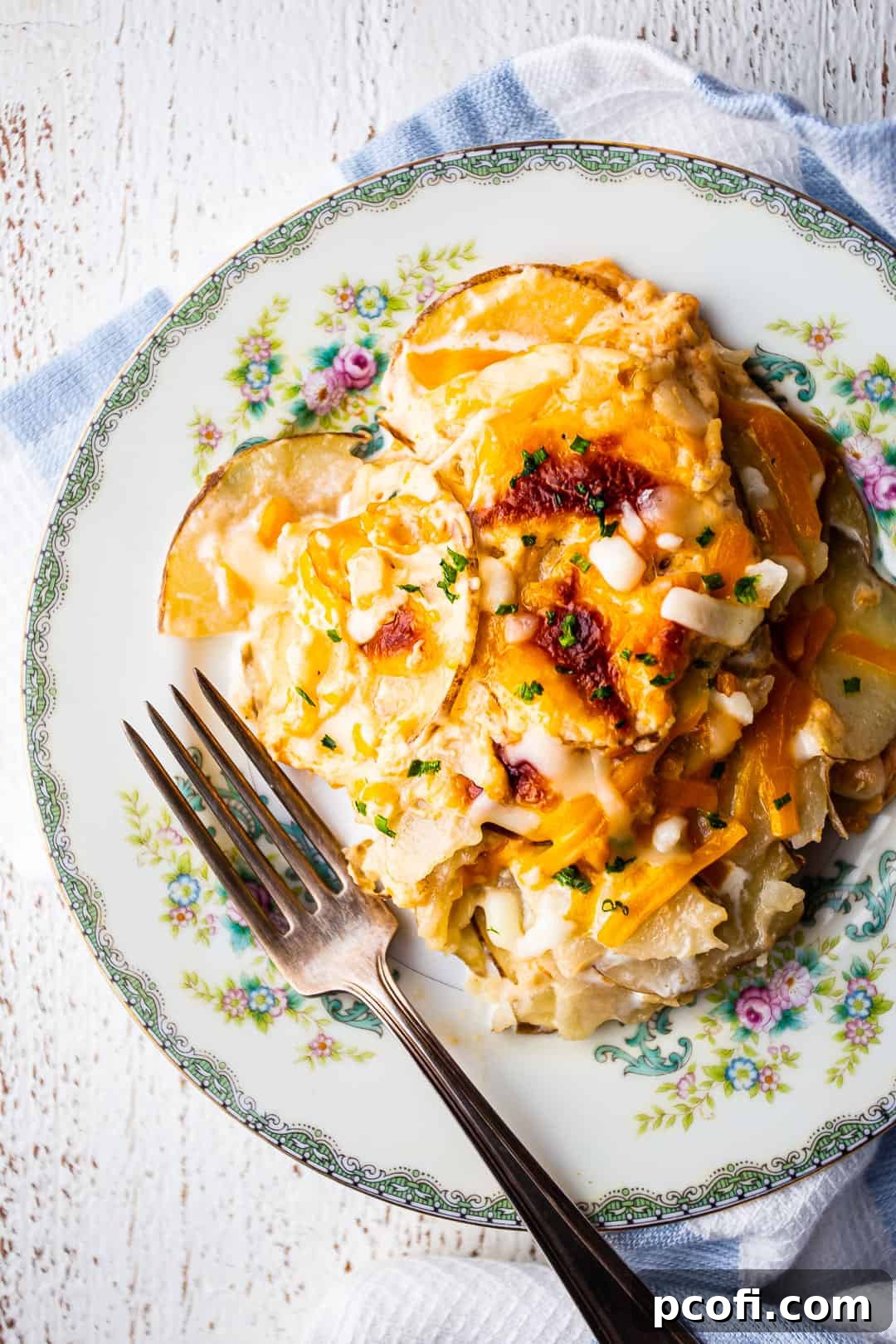 An overhead shot of beautifully prepared scalloped potatoes, served on a floral plate with a blue striped cloth.