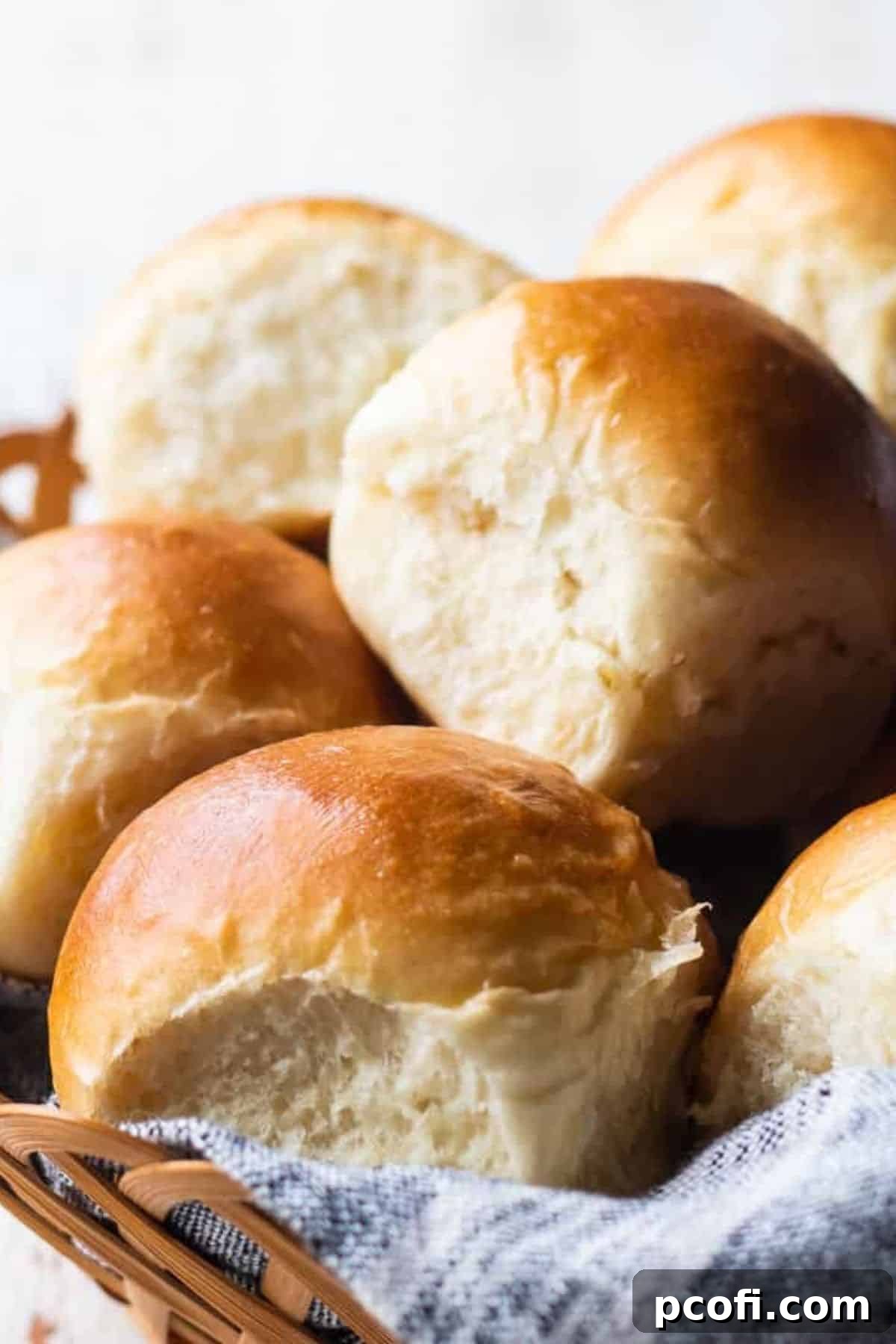 A rustic basket overflowing with golden-brown, soft dinner rolls, artfully arranged with a linen napkin.