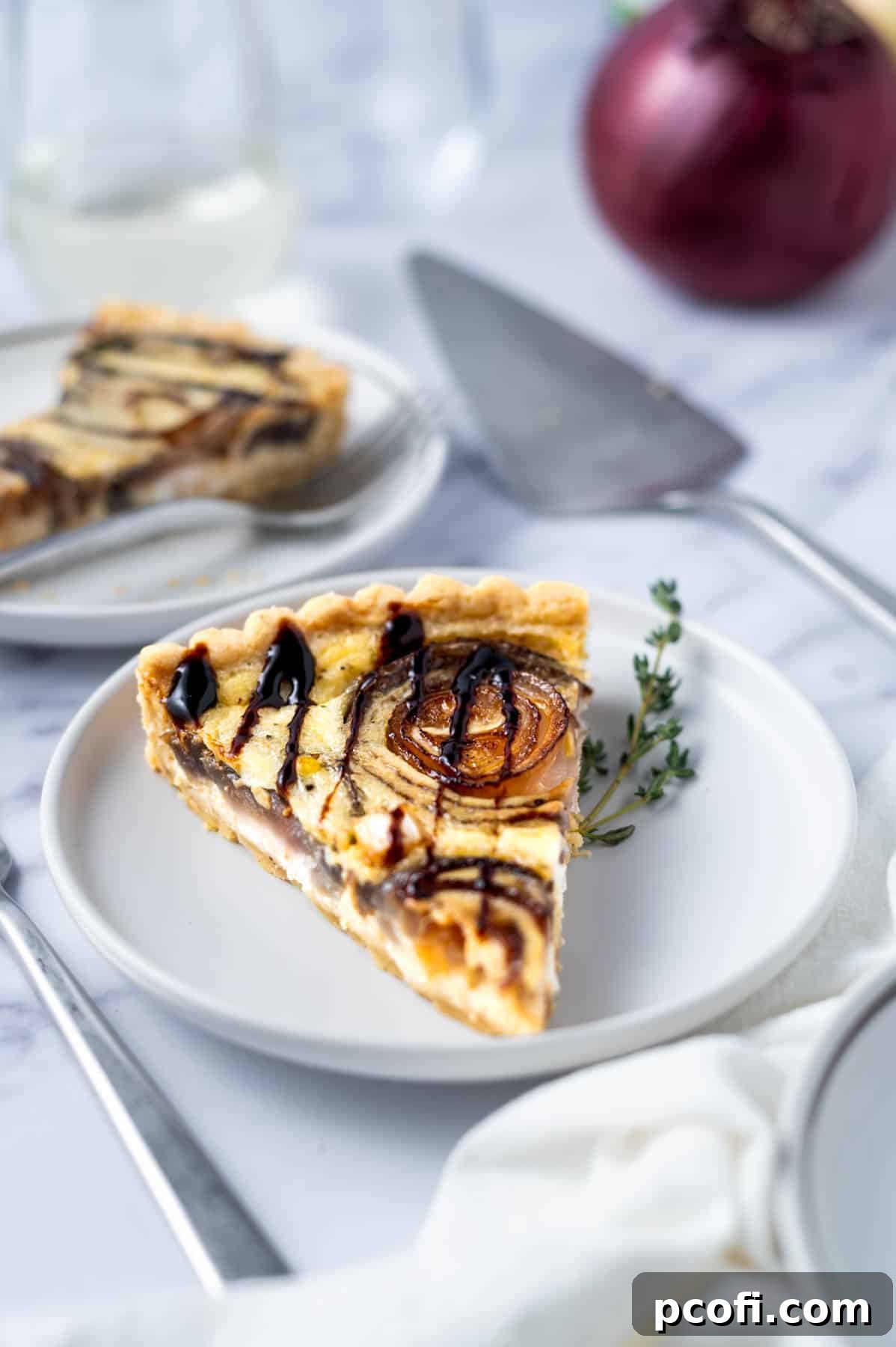 slice of caramelized onion tart on a plate with glasses and onions in the background