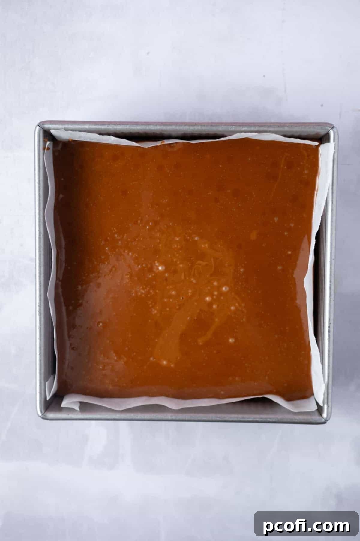 A thick layer of rich caramel spread over the baked shortbread crust in a parchment-lined baking tin, ready for chilling.