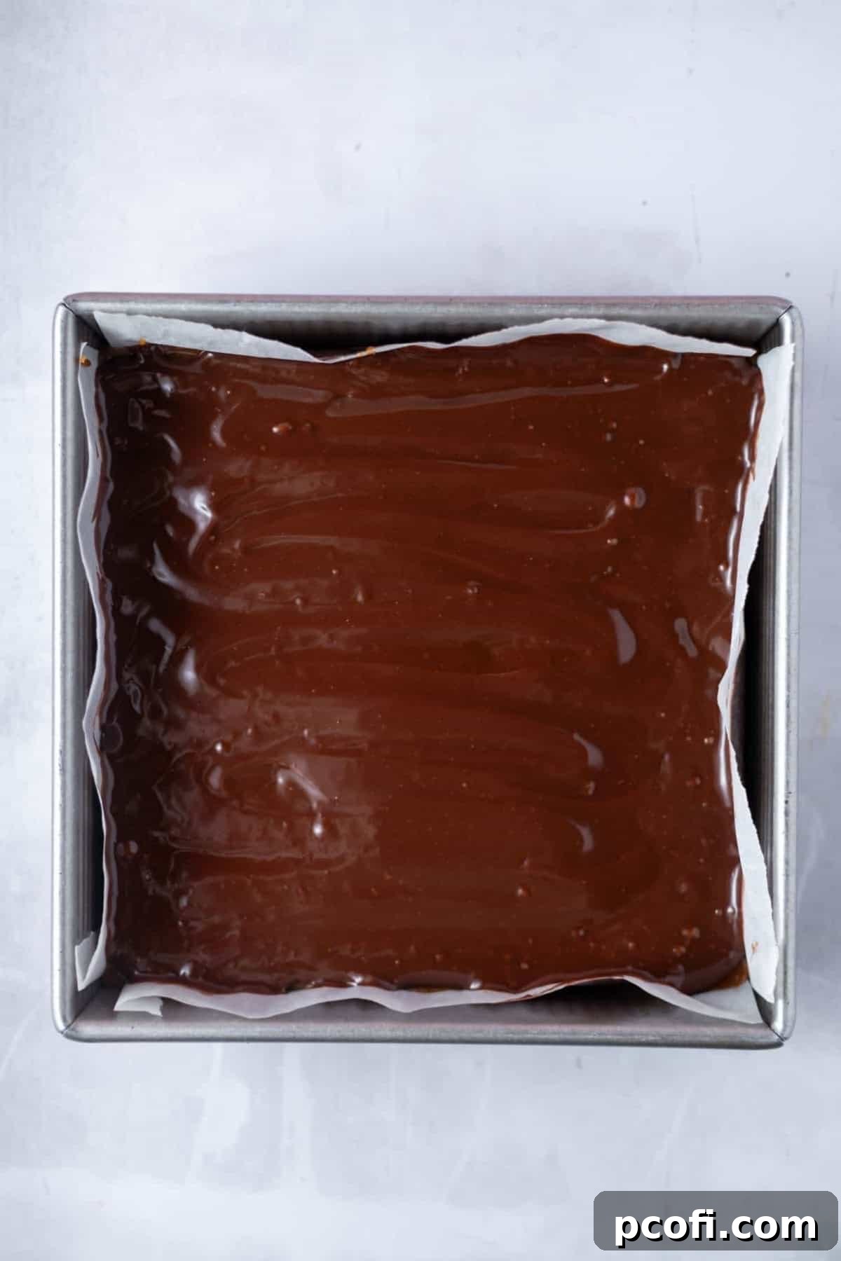 A smooth milk chocolate ganache layer spread evenly on top of the caramel and shortbread, chilling in a parchment-lined baking pan.