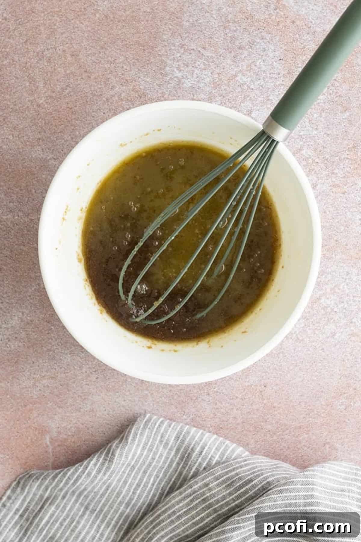 Melted butter and brown sugar being whisked together in a mixing bowl until thoroughly combined.