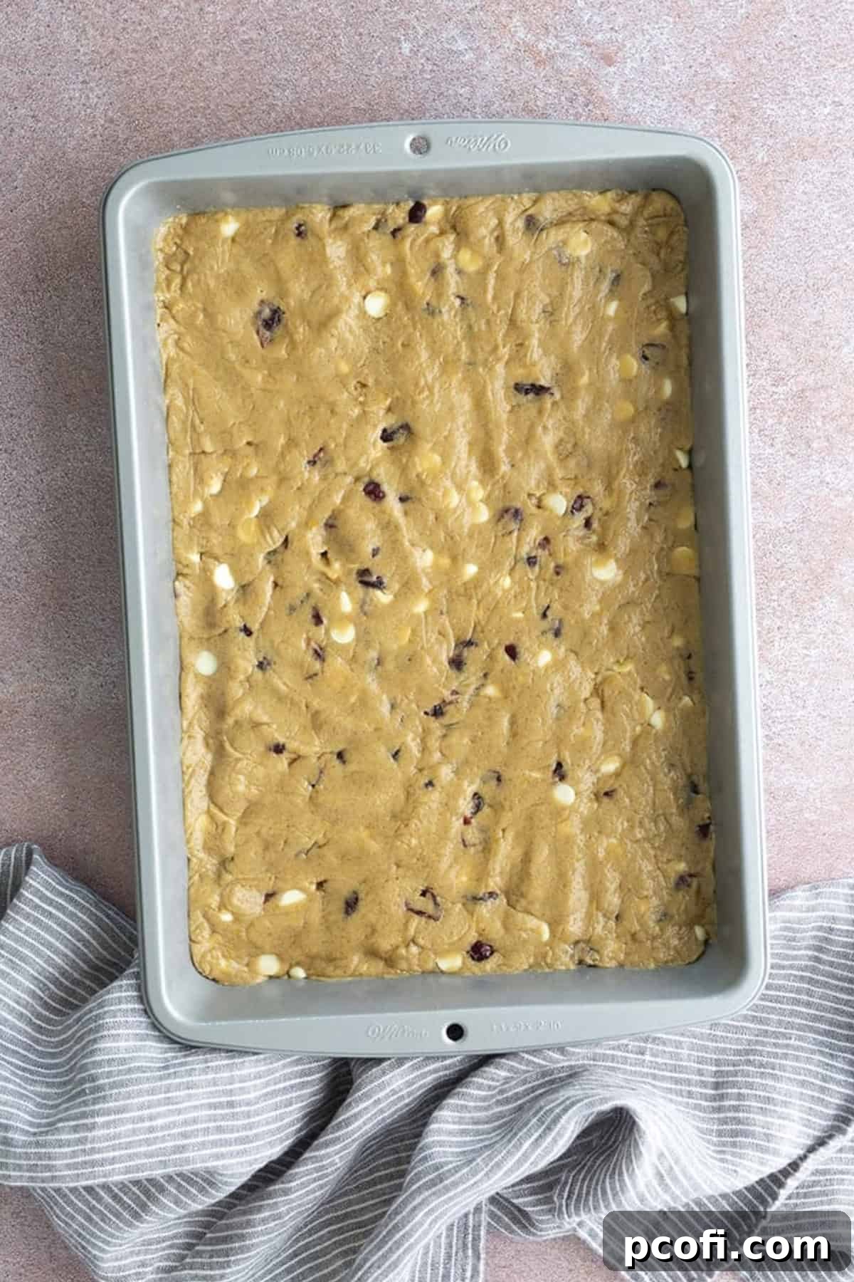 The completed cranberry bliss bar dough evenly spread into a 9x13 inch baking pan, ready for the oven.