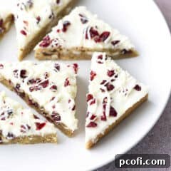 Close-up of cranberry bliss bars cut into perfect triangles on a white plate, highlighting their texture and frosting.