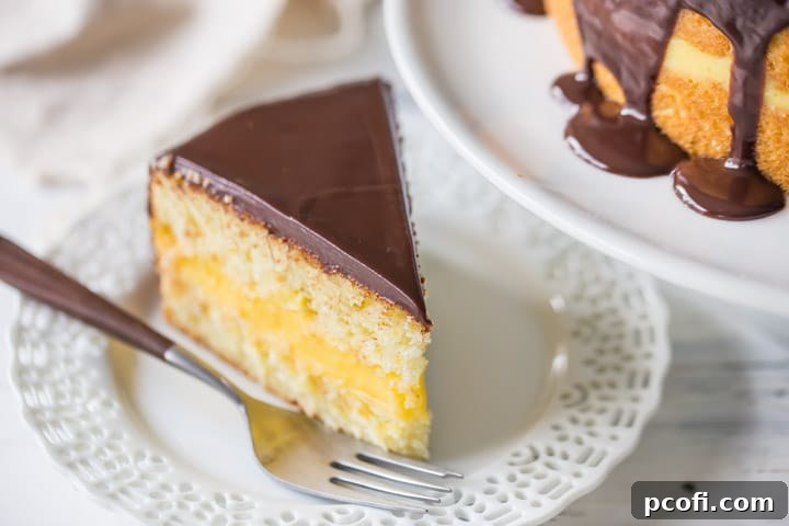 A perfect slice of Boston Cream Pie on a white plate, positioned next to the full cake, showcasing the luscious chocolate ganache topping elegantly dripping down its sides.