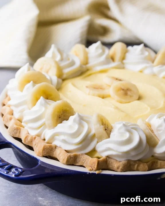 A classic Banana Cream Pie, showcasing a luscious fluffy custard, artful swirls of sweet whipped cream, and layers of fresh bananas, all nestled in a golden crust.