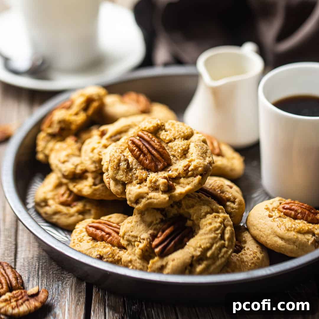 Buttery pecan cookies beautifully arranged in a vintage pie plate, accompanied by a cup of coffee and a small pitcher of cream, setting a cozy and inviting scene.