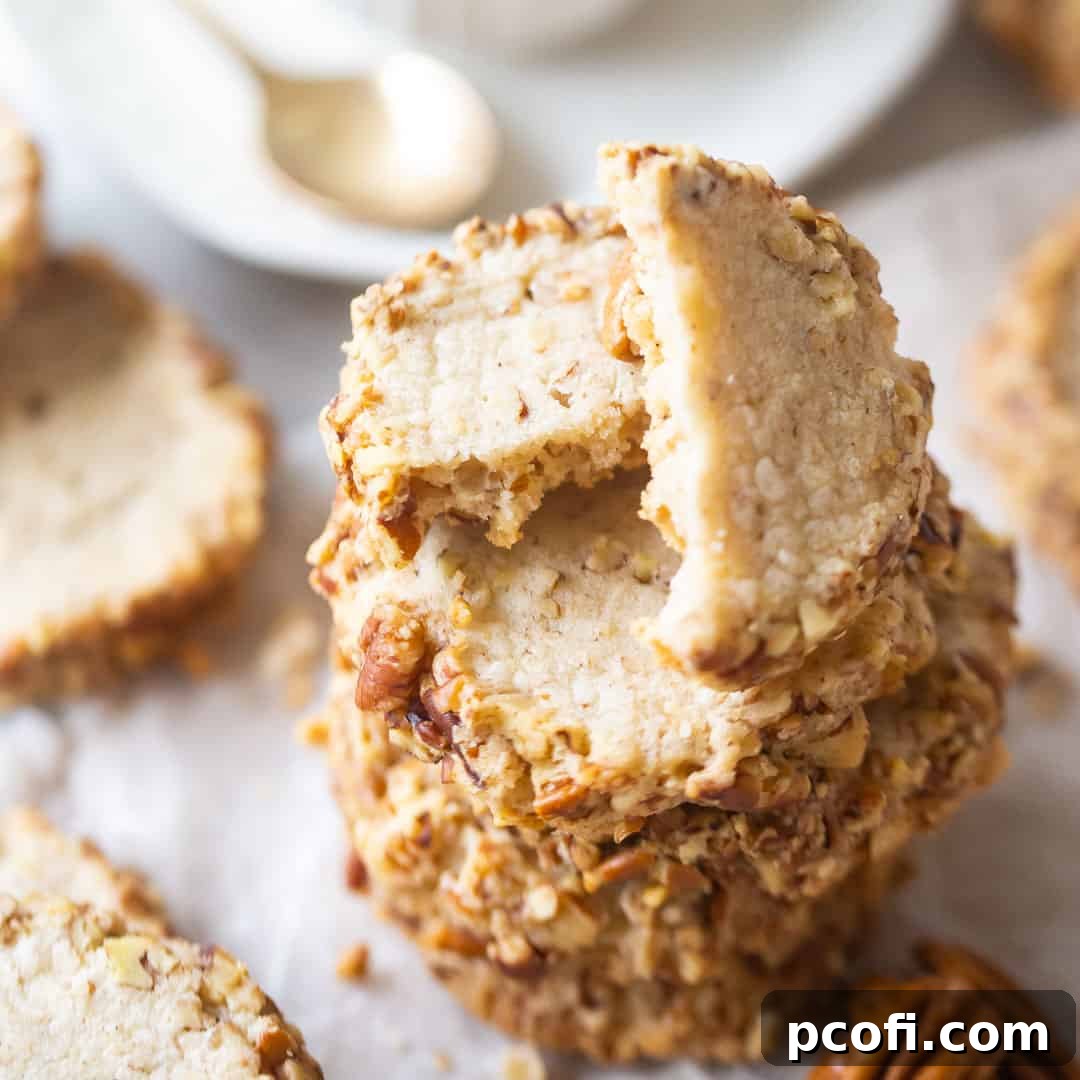 A close-up image of a stack of buttery Pecan Sandies, their edges beautifully rimmed in finely chopped pecans, inviting a delicious bite.