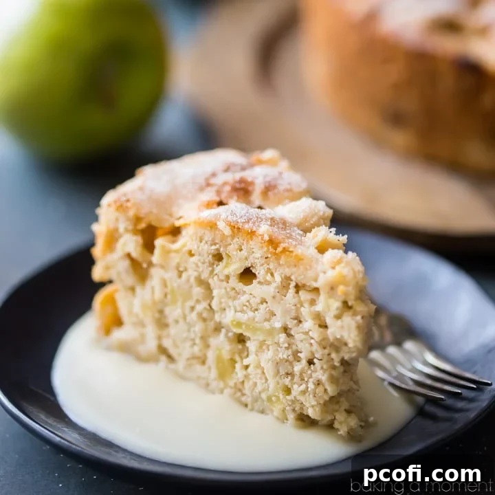 A hearty slice of Irish Apple Cake, served with a creamy whiskey hard sauce. The cake is moist with visible chunks of apple and a hint of cinnamon, offering a comforting and flavorful dessert.
