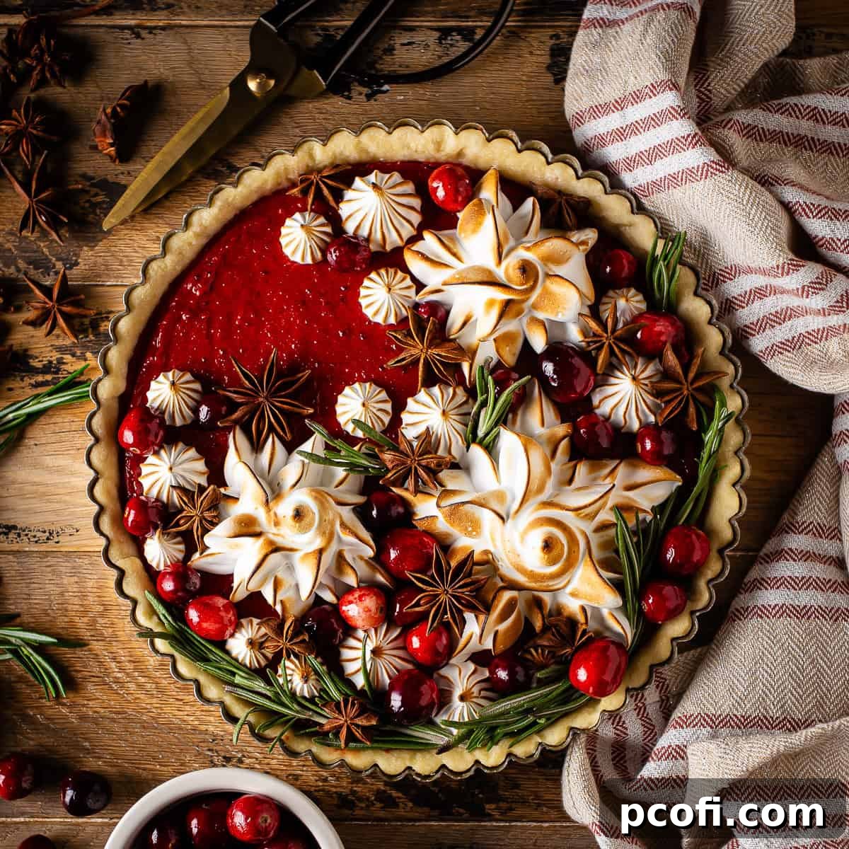 An elegant cranberry curd tart, beautifully topped with delicate toasted meringue peaks and glistening sugared cranberries, ready for a festive display.